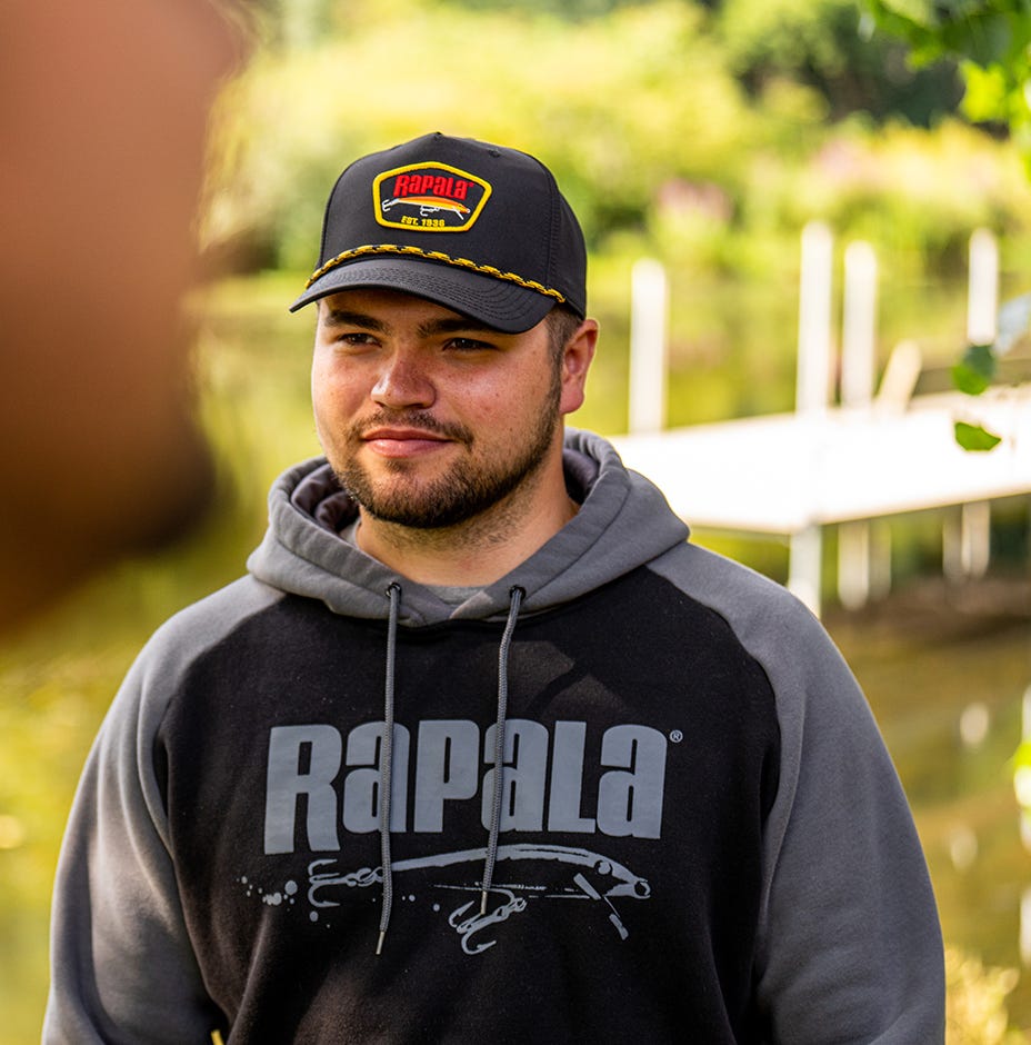 person wearing black and yellow rapala late 80s rope hat near a dock